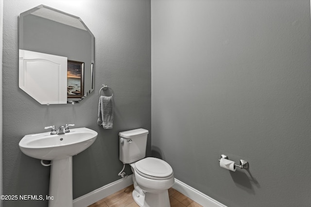 half bath featuring wood finished floors, toilet, and baseboards