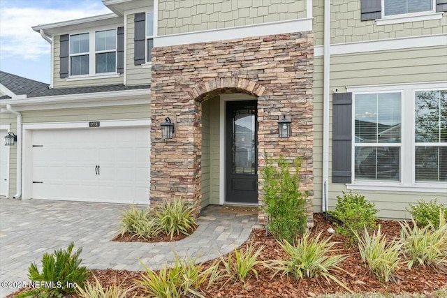 doorway to property with decorative driveway, stone siding, roof with shingles, and an attached garage