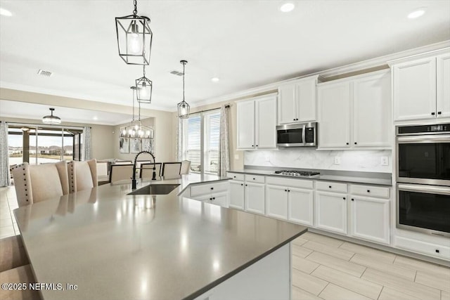 kitchen featuring appliances with stainless steel finishes, backsplash, ornamental molding, a large island with sink, and a sink