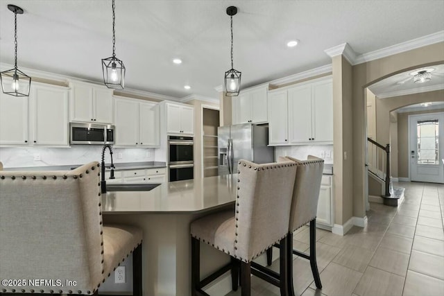 kitchen featuring arched walkways, stainless steel appliances, a breakfast bar, decorative backsplash, and crown molding