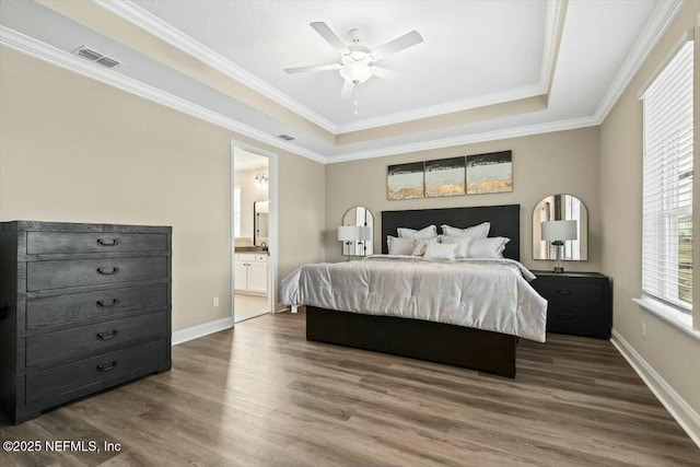 bedroom featuring baseboards, a tray ceiling, visible vents, and wood finished floors