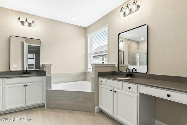 full bath featuring a stall shower, two vanities, a sink, and a bath