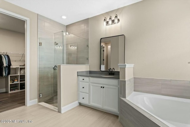 full bathroom with a stall shower, wood finished floors, a garden tub, a walk in closet, and vanity