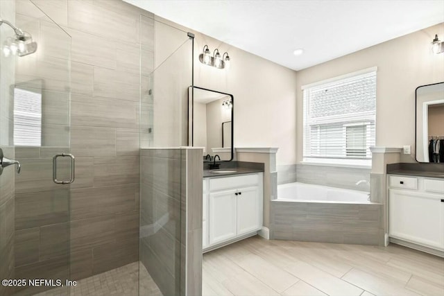 full bath featuring two vanities, a stall shower, a garden tub, and a sink