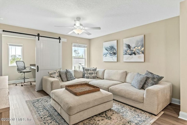 living room with a textured ceiling, a barn door, wood finished floors, a ceiling fan, and baseboards