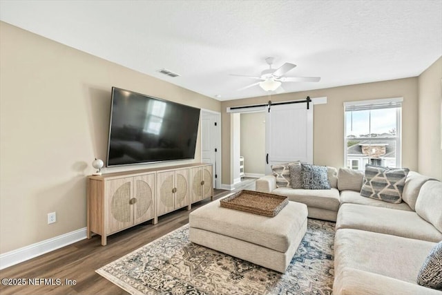 living room with visible vents, a barn door, a ceiling fan, wood finished floors, and baseboards