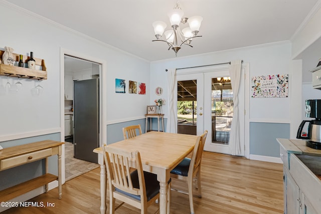 dining area featuring light wood finished floors, ornamental molding, a notable chandelier, and french doors