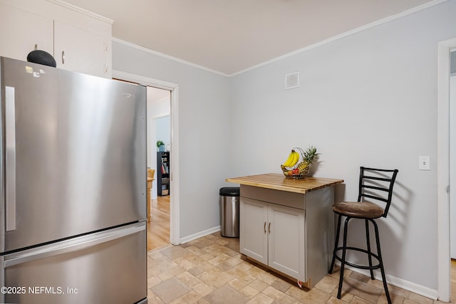 kitchen featuring baseboards, butcher block counters, freestanding refrigerator, stone finish flooring, and crown molding