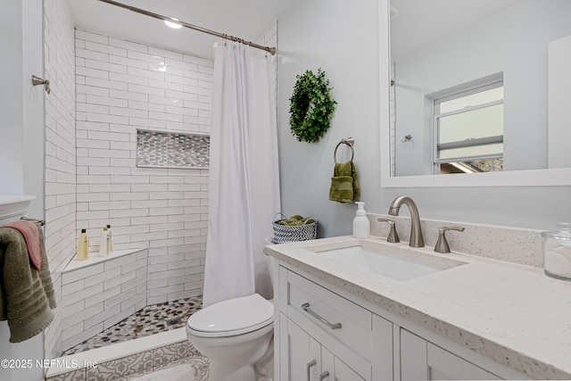 bathroom featuring toilet, tiled shower, and vanity