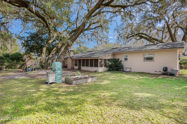 rear view of property with a sunroom, a playground, and a yard