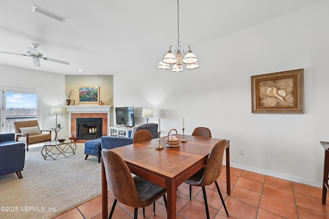 dining area featuring visible vents, light tile patterned flooring, a tile fireplace, baseboards, and ceiling fan with notable chandelier