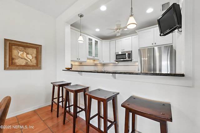 kitchen with stainless steel appliances, glass insert cabinets, decorative backsplash, and a breakfast bar area