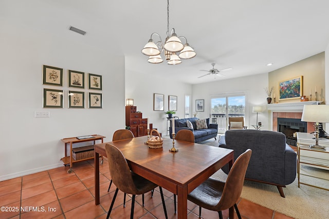 tiled dining area with baseboards, visible vents, a tiled fireplace, and ceiling fan with notable chandelier