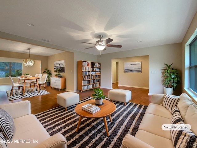 living area with ceiling fan with notable chandelier, wood finished floors, and baseboards