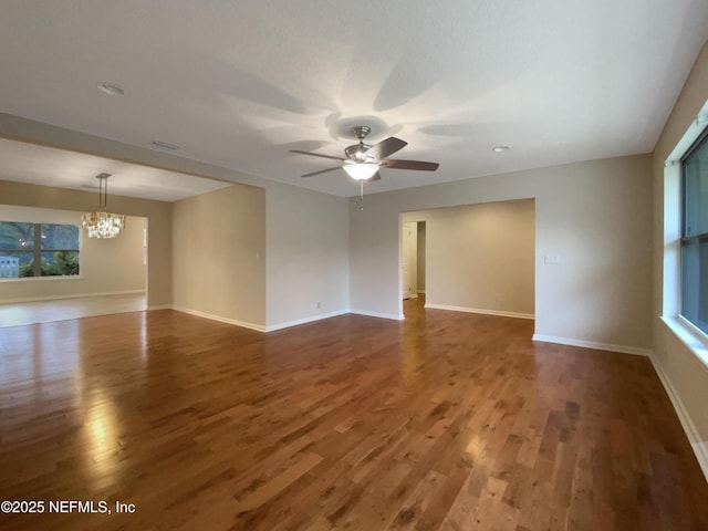 unfurnished room with dark wood-type flooring, a healthy amount of sunlight, baseboards, and ceiling fan with notable chandelier