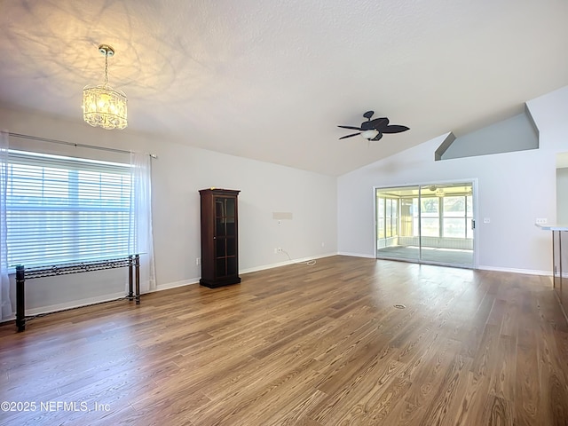 unfurnished living room with wood finished floors, baseboards, lofted ceiling, a textured ceiling, and ceiling fan with notable chandelier