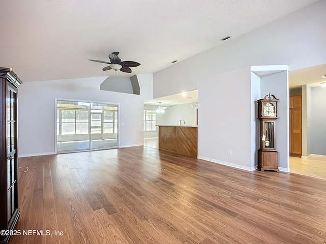 unfurnished living room with baseboards, high vaulted ceiling, wood finished floors, and a ceiling fan