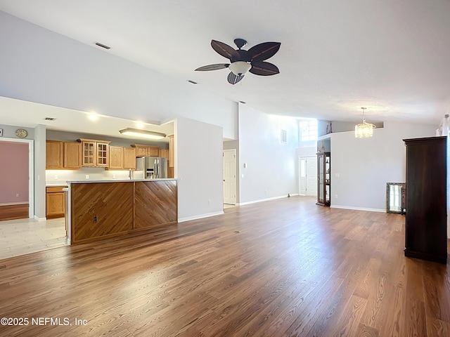 unfurnished living room with light wood-style flooring, baseboards, high vaulted ceiling, and ceiling fan