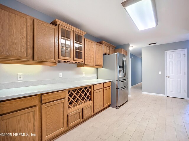 kitchen featuring visible vents, stainless steel refrigerator with ice dispenser, light countertops, glass insert cabinets, and baseboards