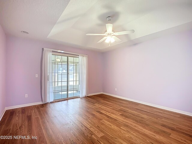 spare room featuring a ceiling fan, a raised ceiling, baseboards, and wood finished floors