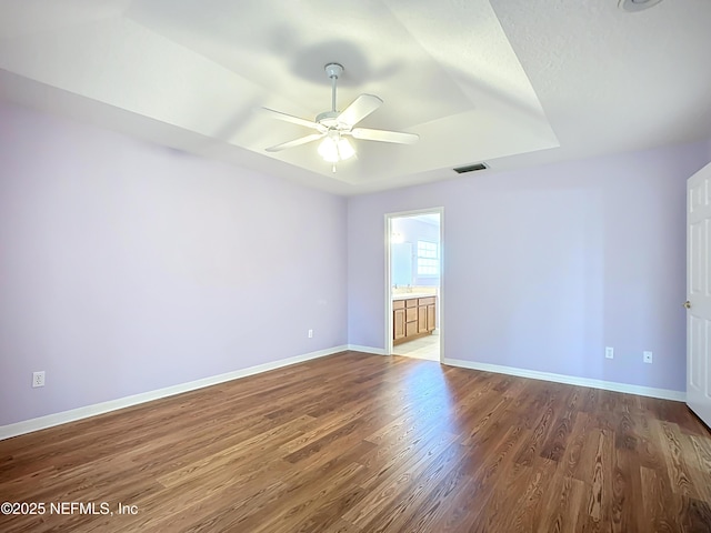 unfurnished room with dark wood-style floors, visible vents, baseboards, a tray ceiling, and ceiling fan