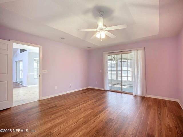 spare room featuring ceiling fan, baseboards, a raised ceiling, and wood finished floors