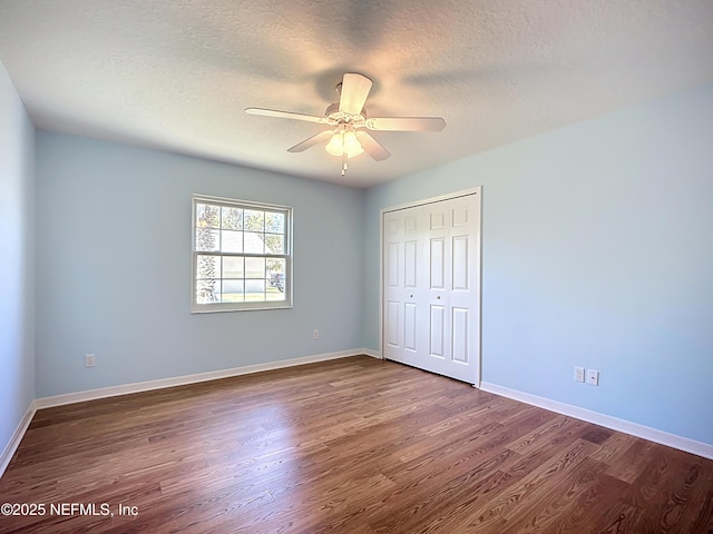 unfurnished bedroom featuring dark wood-type flooring, ceiling fan, baseboards, a closet, and a textured ceiling