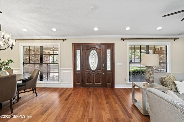 entryway featuring a notable chandelier, wainscoting, wood finished floors, and crown molding