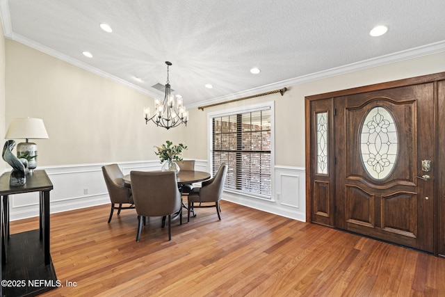 dining space featuring crown molding, a textured ceiling, a chandelier, and light wood-style floors