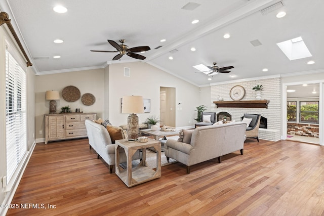 living room featuring visible vents, ornamental molding, lofted ceiling with skylight, a brick fireplace, and light wood-type flooring