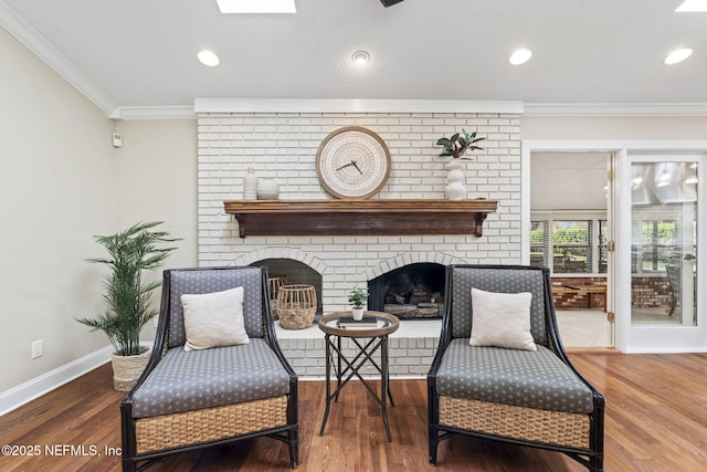 living area featuring baseboards, wood finished floors, crown molding, a brick fireplace, and recessed lighting