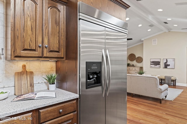 kitchen featuring vaulted ceiling with beams, crown molding, built in refrigerator, light wood finished floors, and tasteful backsplash