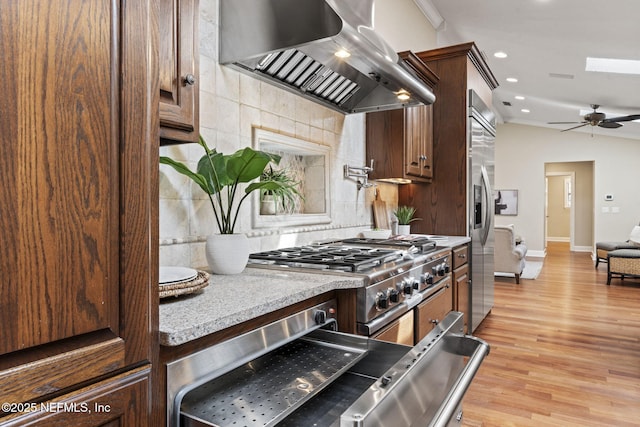 kitchen with light wood finished floors, tasteful backsplash, stainless steel built in refrigerator, range, and extractor fan