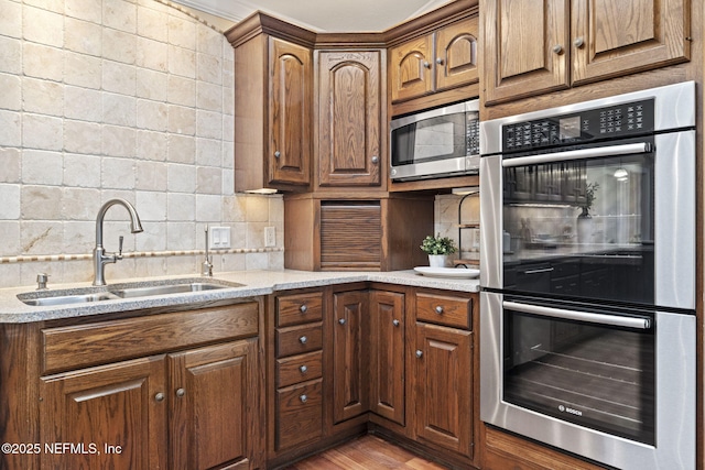 kitchen with light wood finished floors, stainless steel appliances, decorative backsplash, a sink, and light stone countertops