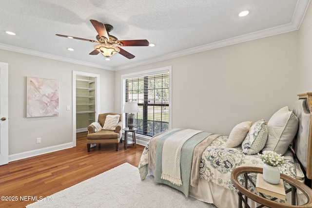 bedroom with a spacious closet, a textured ceiling, ornamental molding, and wood finished floors