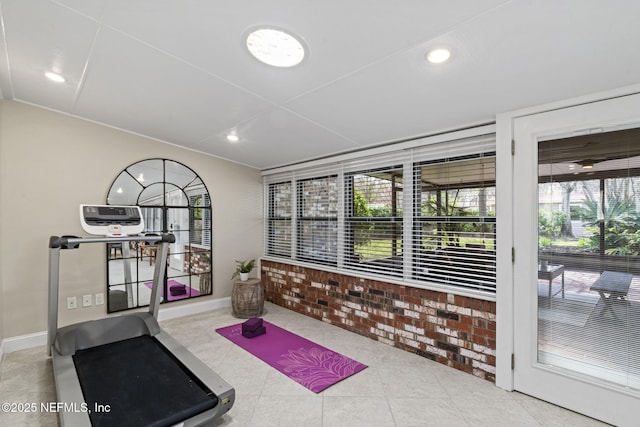 exercise area featuring a sunroom, brick wall, baseboards, and tile patterned floors