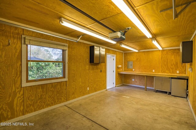 garage featuring a garage door opener, wooden walls, baseboards, and fridge