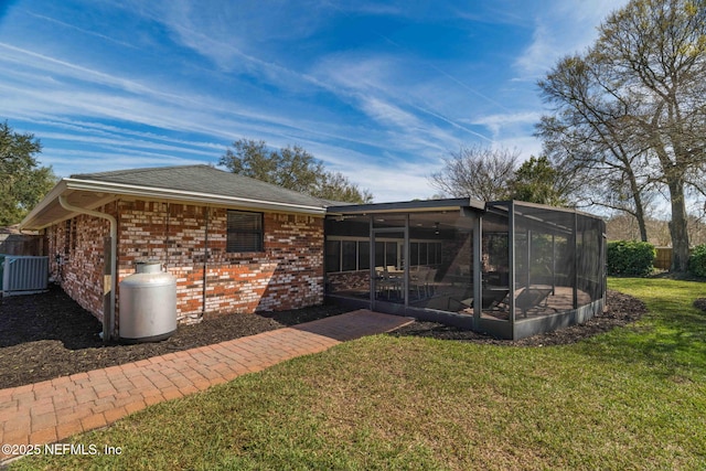 rear view of property featuring central AC, brick siding, a lawn, and a sunroom