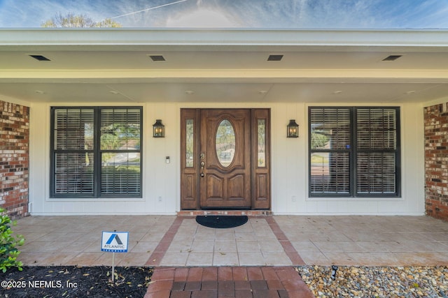 entrance to property with a porch, brick siding, and visible vents