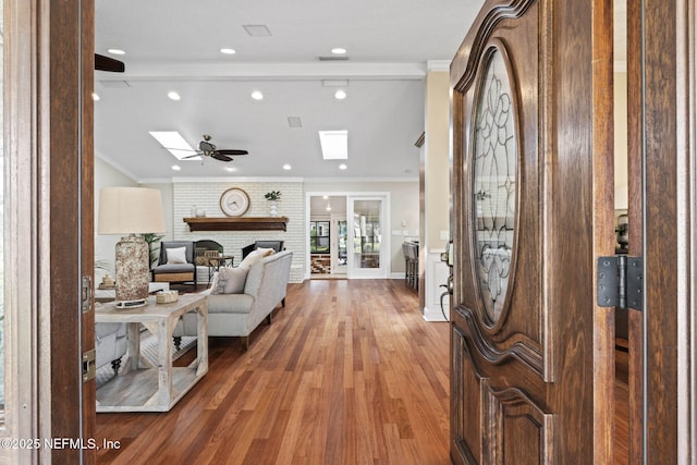 entrance foyer featuring baseboards, a ceiling fan, light wood-style flooring, ornamental molding, and a fireplace