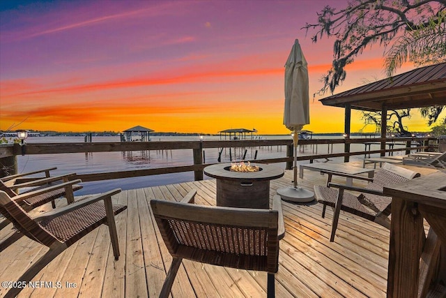 deck at dusk featuring a water view, a fire pit, and a gazebo