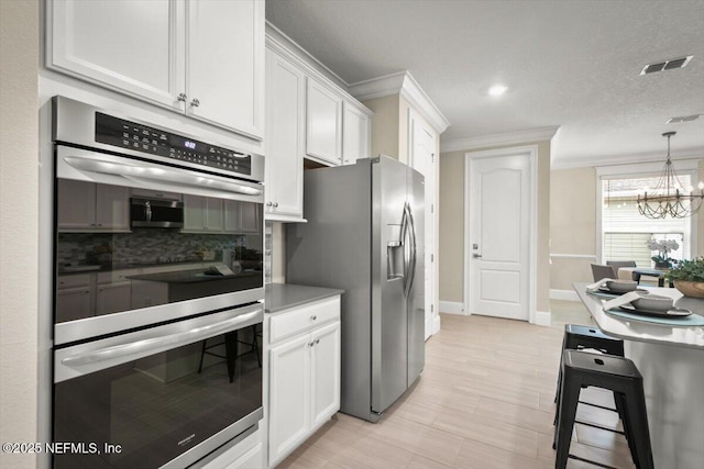 kitchen with stainless steel appliances, white cabinets, ornamental molding, and decorative backsplash