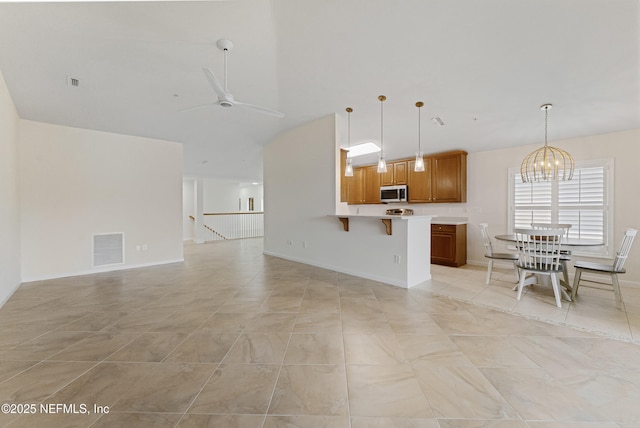 kitchen featuring open floor plan, stainless steel microwave, brown cabinetry, and visible vents