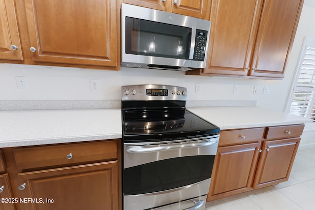 kitchen featuring light tile patterned floors, light countertops, appliances with stainless steel finishes, and brown cabinets