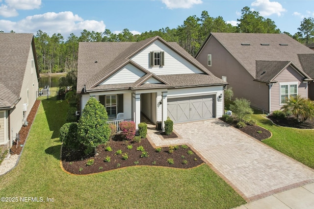 view of front facade featuring roof with shingles, an attached garage, decorative driveway, a porch, and a front yard