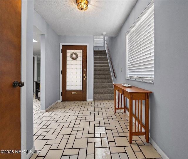 entryway with a textured ceiling, baseboards, and stairs