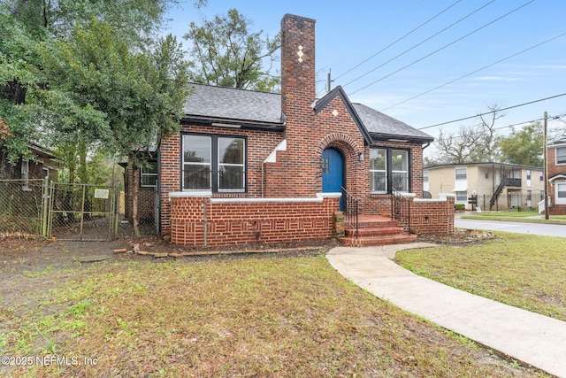 tudor home with a chimney, roof with shingles, fence, a front lawn, and brick siding