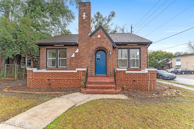 view of front of property featuring roof with shingles, brick siding, a chimney, and fence