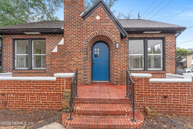 view of front facade with a shingled roof, a chimney, and brick siding