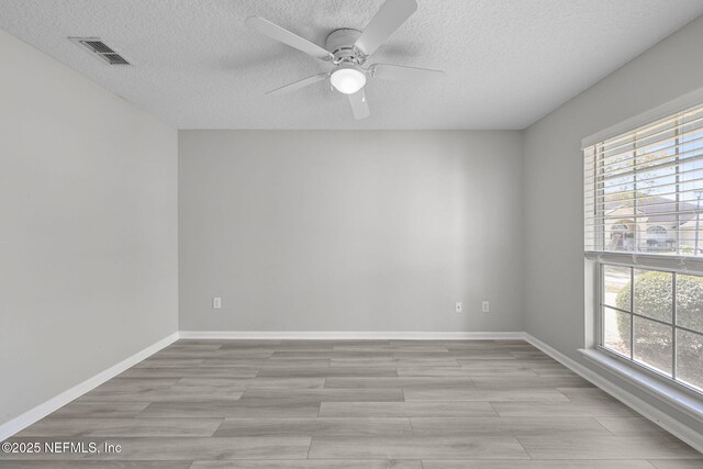 empty room featuring visible vents, light wood-style floors, a ceiling fan, a textured ceiling, and baseboards